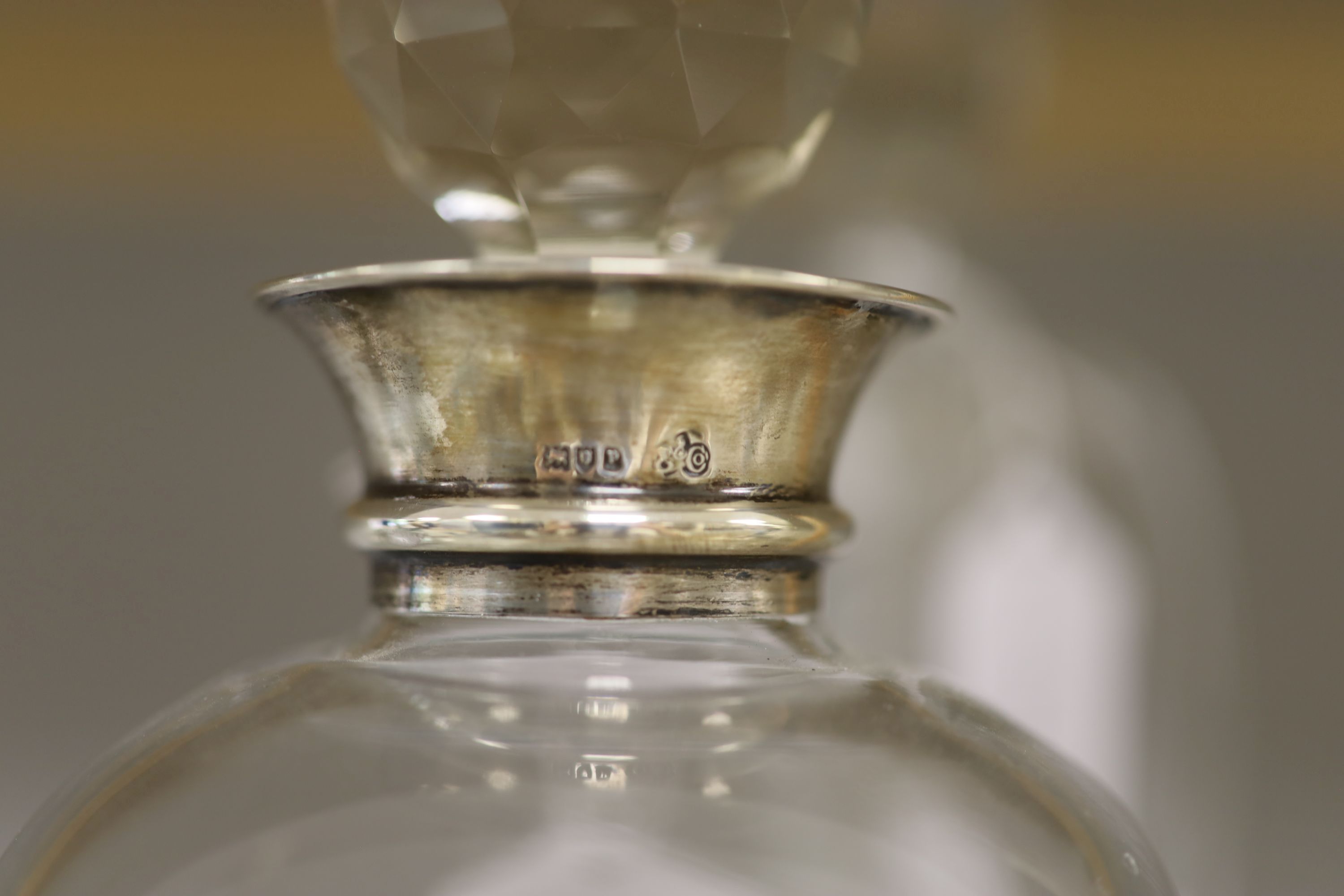 A George V silver collared decanter, a facet cut glass decanter and a wheel engraved glass claret jug with associated stopper, tallest